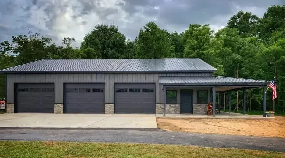 Modern gray garage with three doors and a covered porch in a wooded rural setting