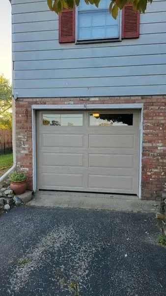 House exterior with a beige garage door, brick trim, white siding, and a driveway in front