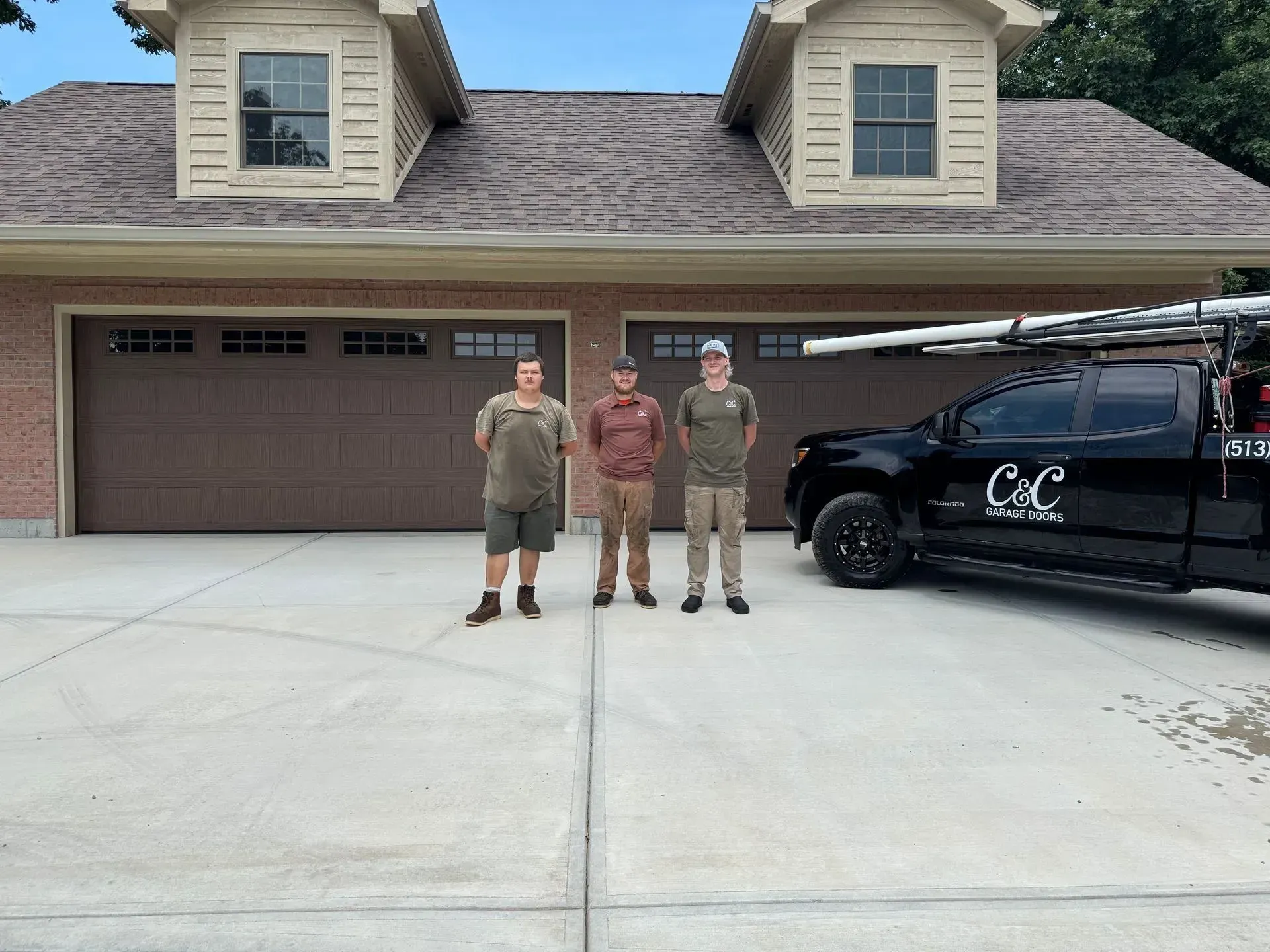 Three people stand in a driveway before a garage, next to a black work truck.