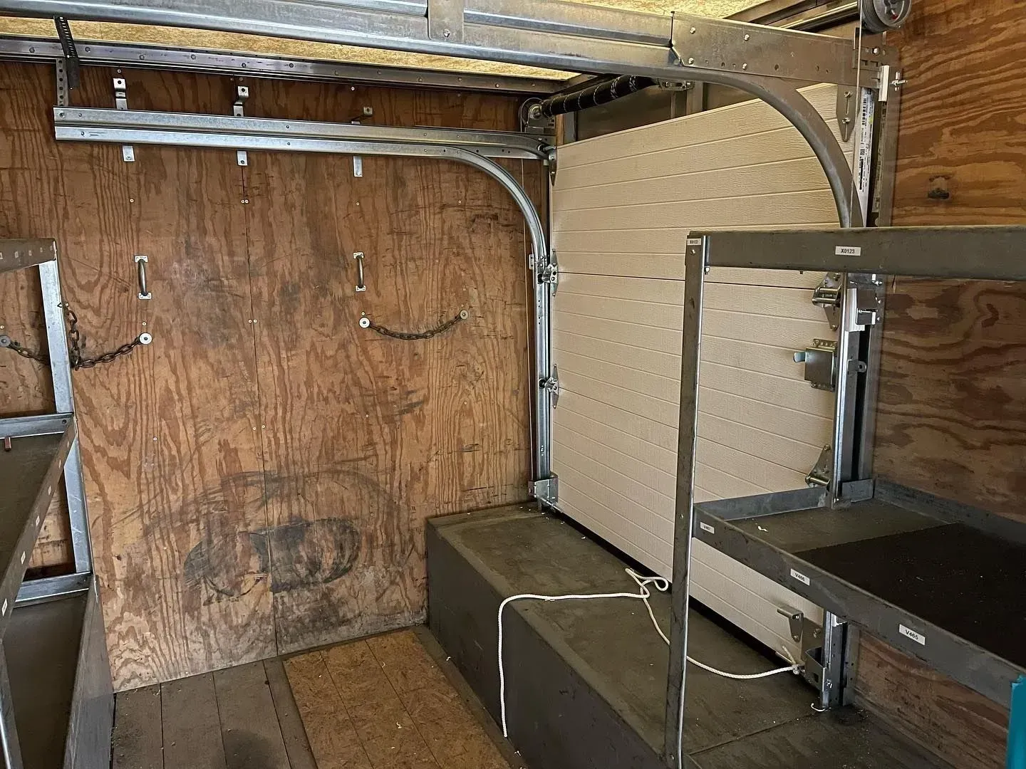 Storage area with plywood wall, metal shelving, and a large bench seat under exposed pipes.