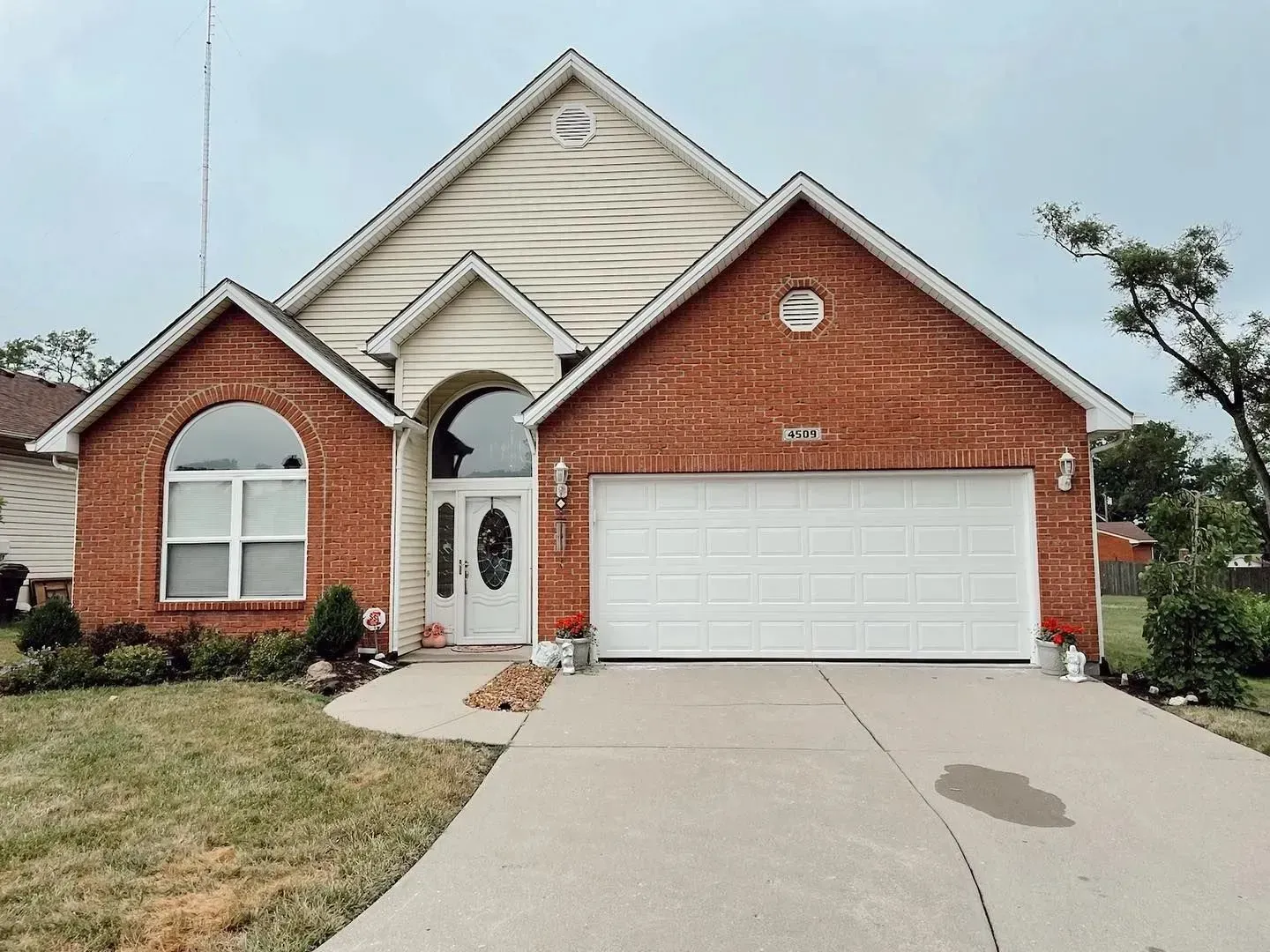Suburban brick-and-siding house with white garage door and arched front entry, viewed from driveway