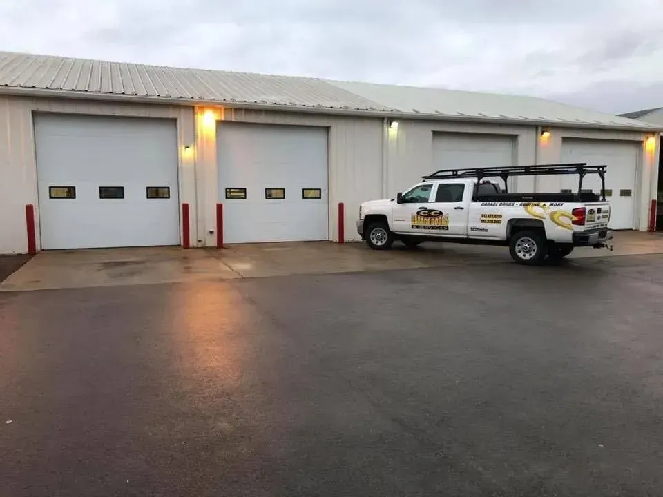 White service truck parked outside a gray industrial garage with three bay doors at dusk