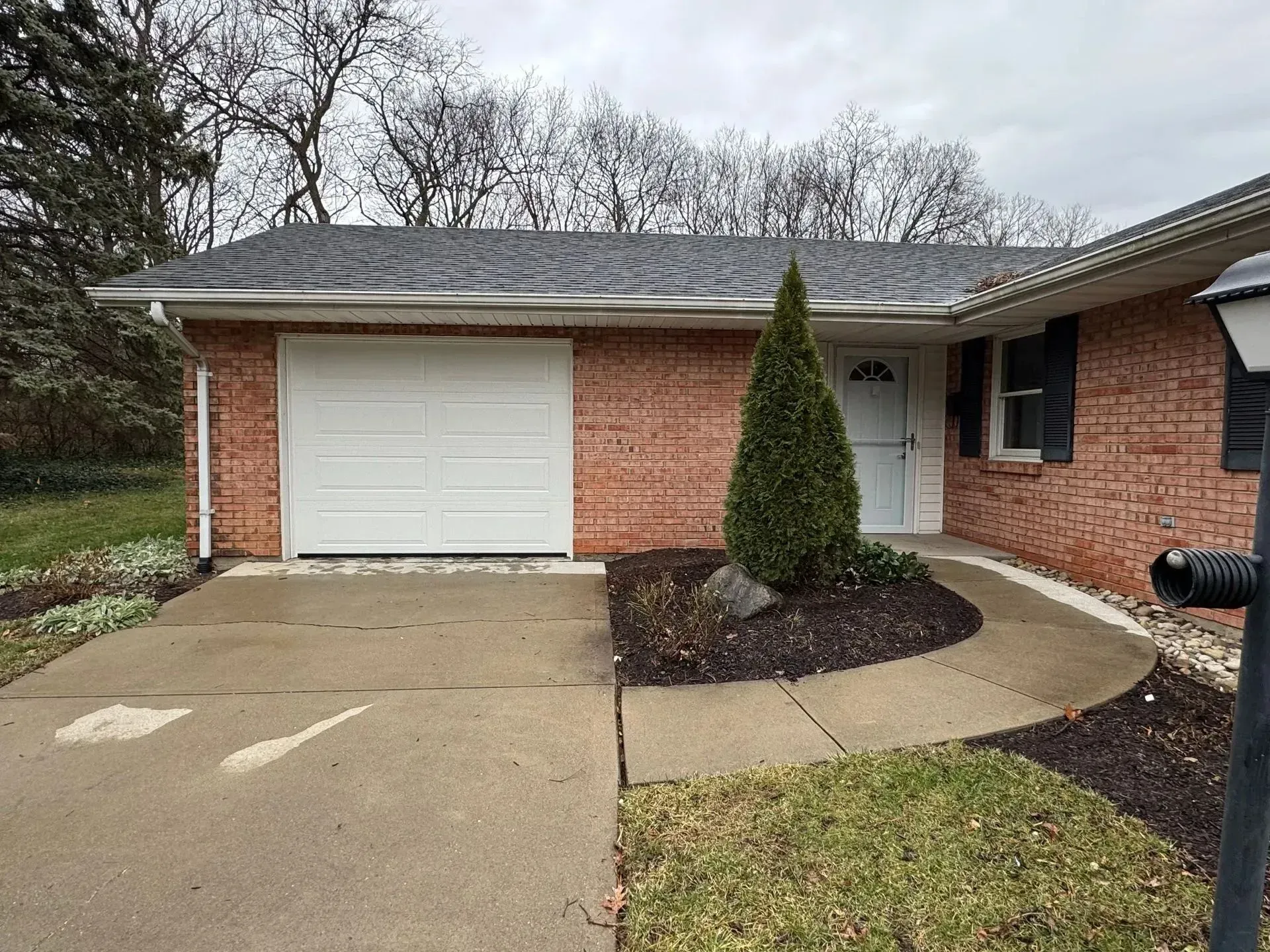 Brick single-story house with white garage door and curved concrete walkway by a small front yard
