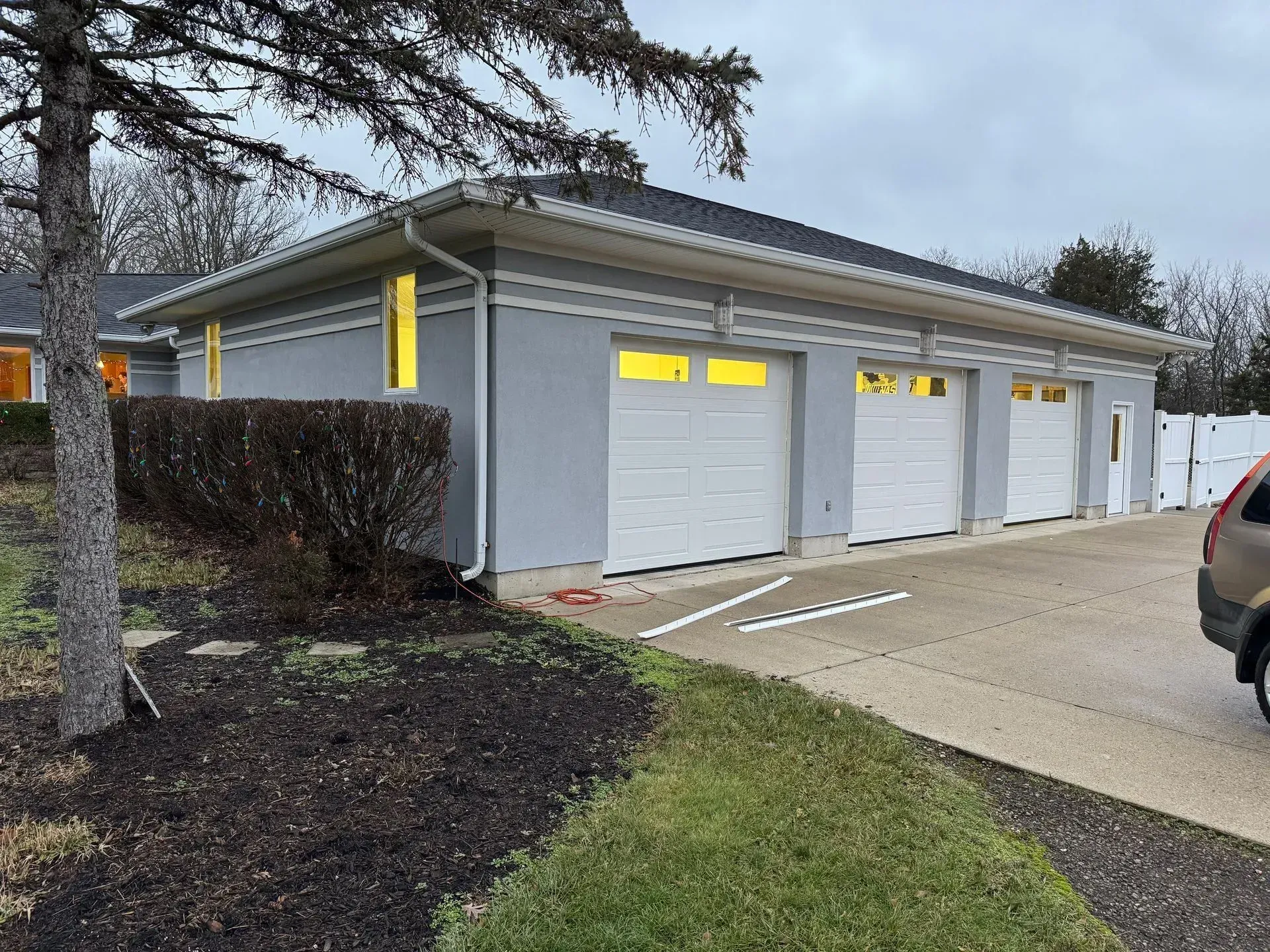 Row of gray garage units with closed white doors beside a driveway and hedges