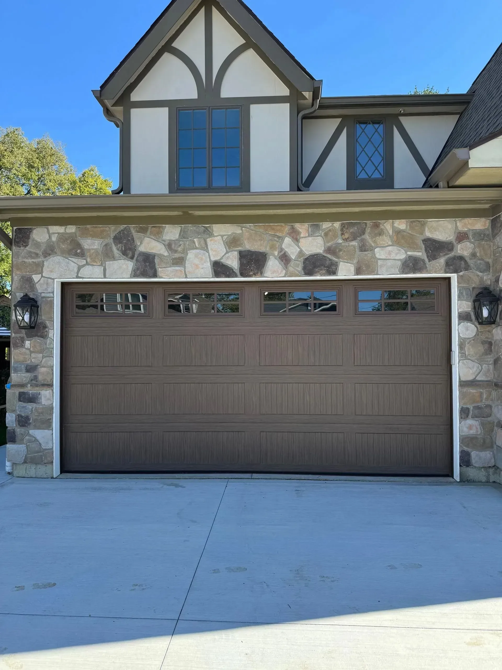 Two-story house with a brown garage door, stone accents, and a blue sky above.