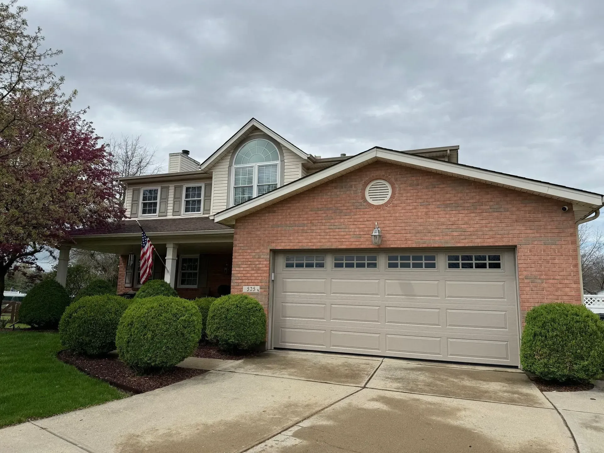 Suburban brick house with two-car garage, driveway, and manicured front yard under cloudy sky