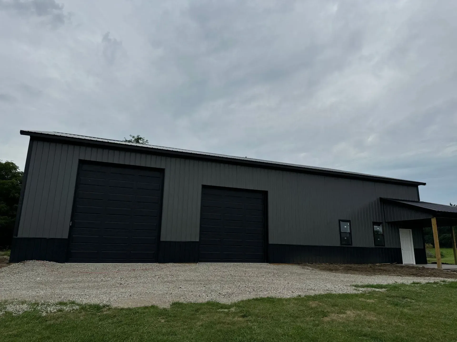 Gray metal warehouse with two large black garage doors under an overcast sky