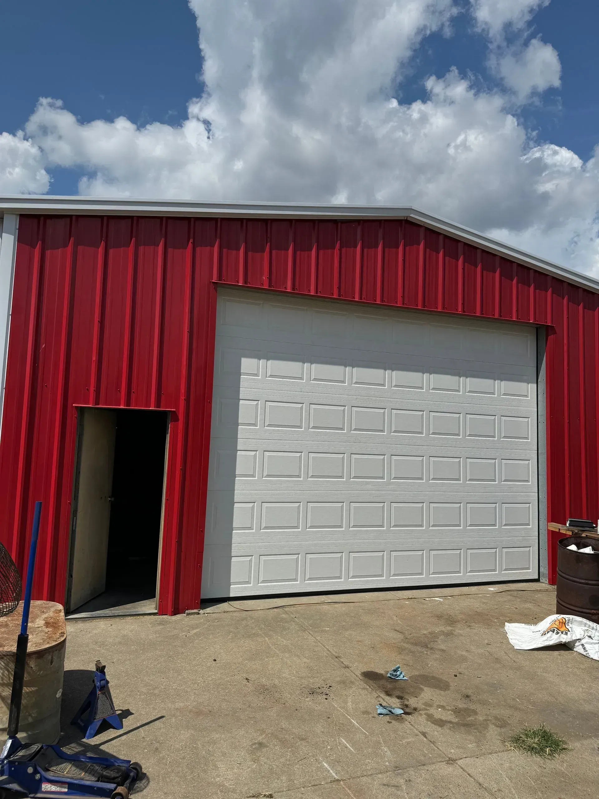 Red metal garage with white roll-up door under a cloudy sky on a gravel lot