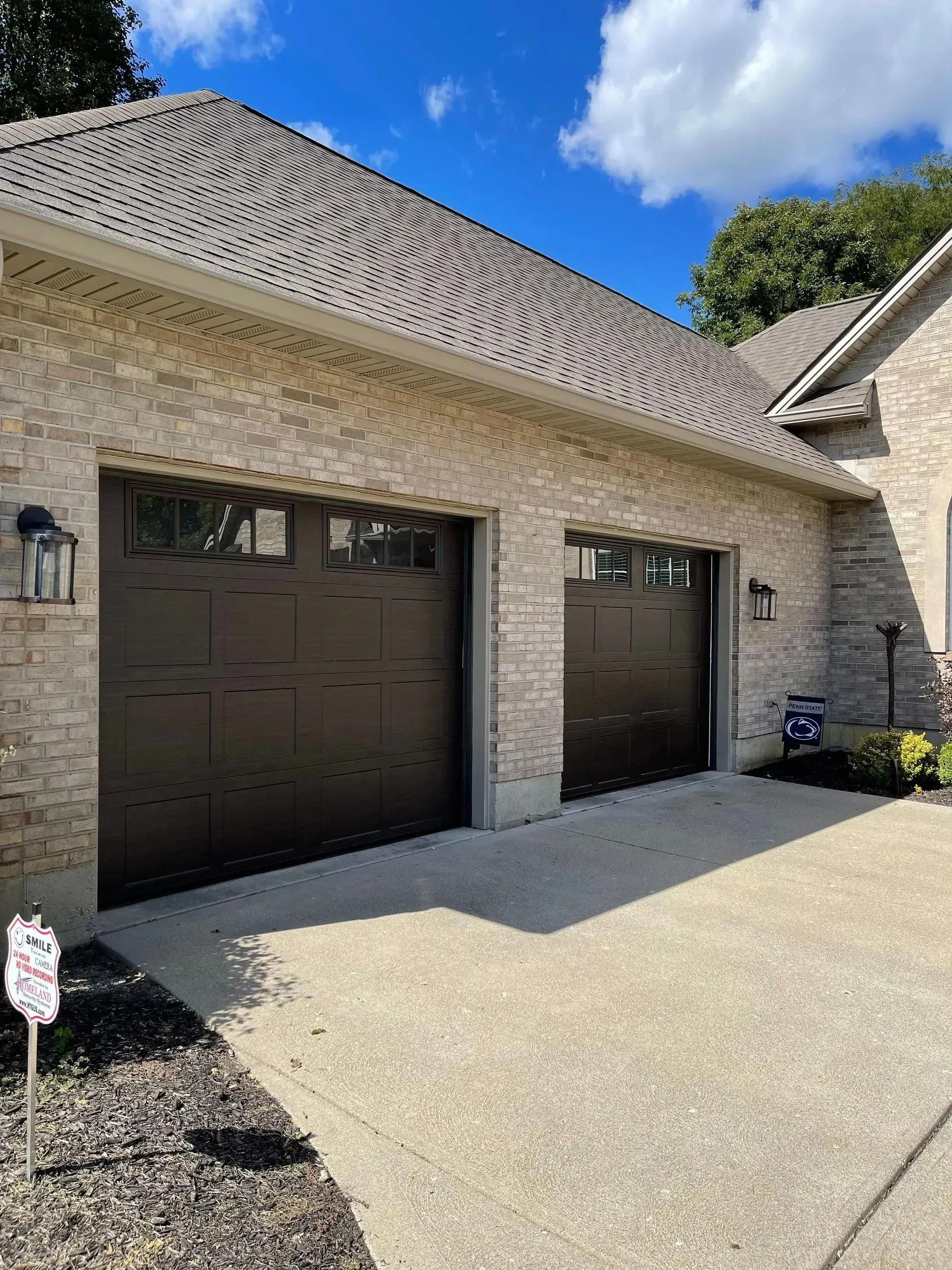 Brick house garage with two dark brown doors and a concrete driveway under a blue sky