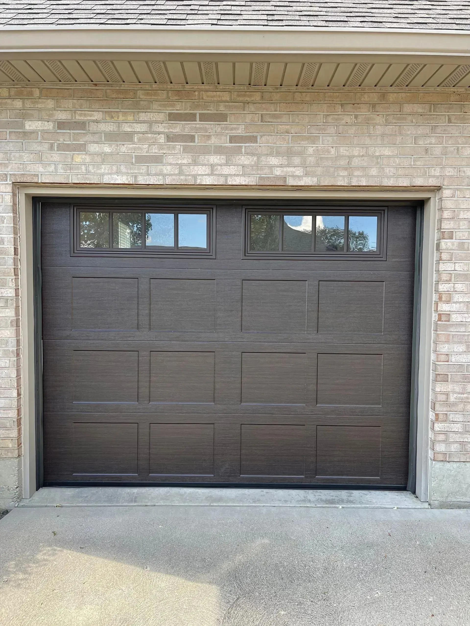 Dark brown garage door with small windows in a beige brick exterior.