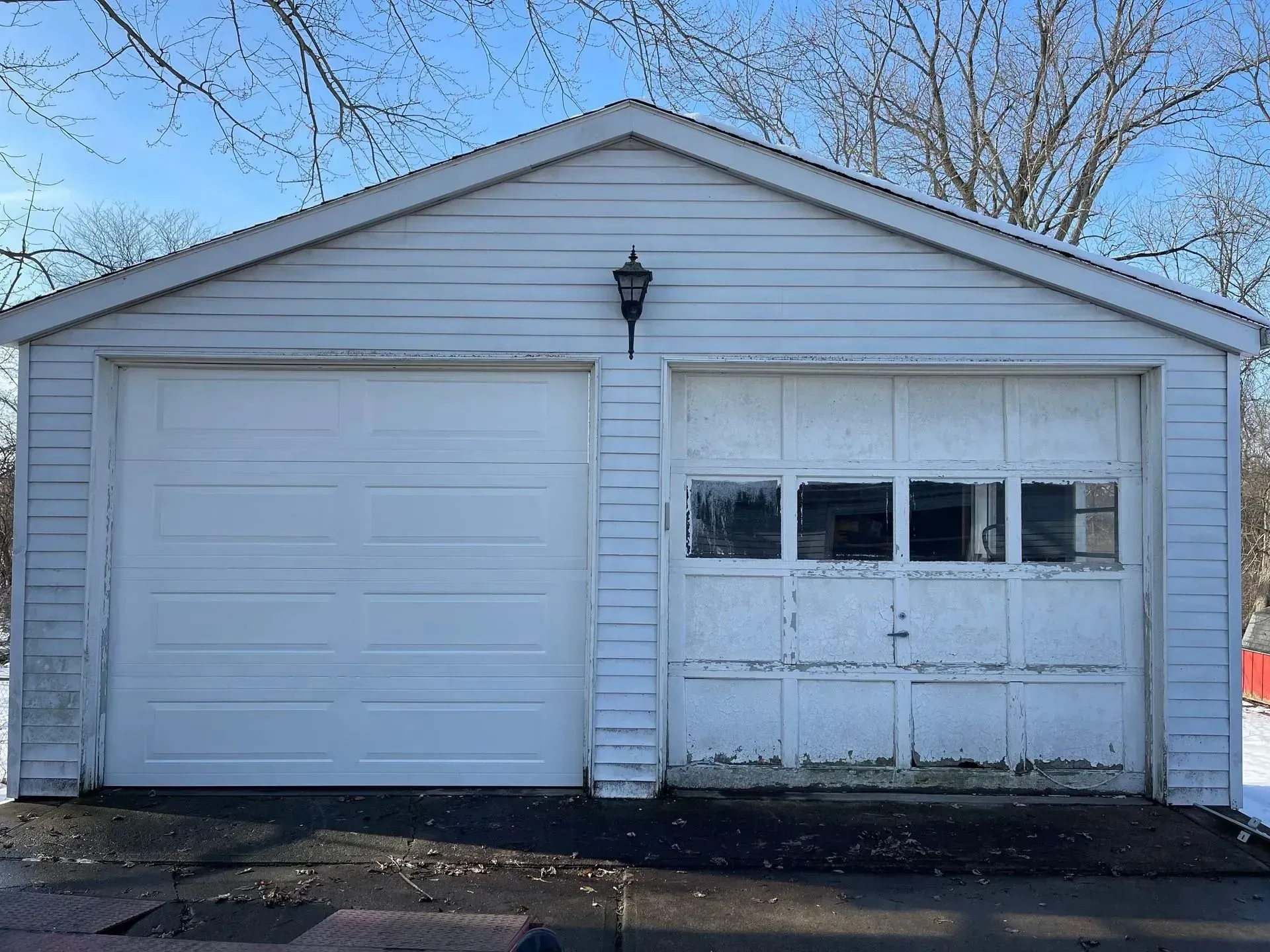 White detached garage with one regular door and one garage door under a peaked roof.