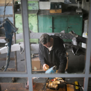 Person in a workshop bends over a workbench, using a tool on a brass machine part.