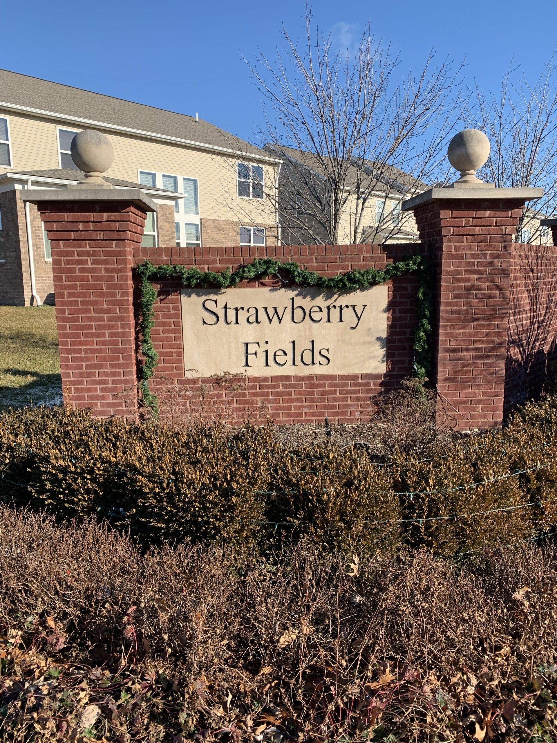 Brick entrance sign reading “Strawberry Fields” beside apartment buildings in daylight