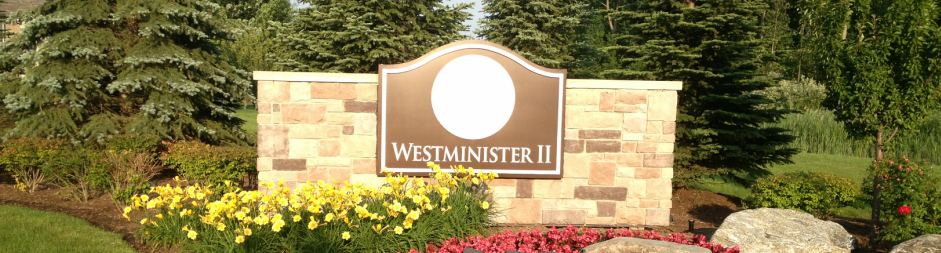 Stone entrance sign for Westminster II, surrounded by trees, shrubs, and red flowers.