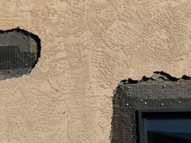 “Close-up of broken stucco with dark exposed underlayment showing areas that need repair during a stucco service in Spring Valley, NV”