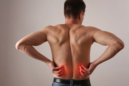 Man holding lower back with red highlighted pain areas, seen from behind.