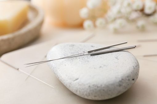 White pebble with thin acupuncture needles on a soft beige spa background