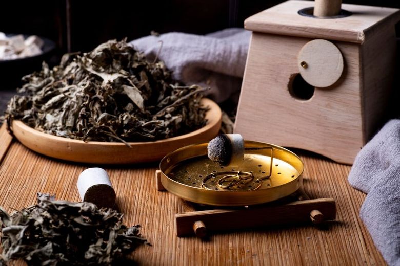 Tea setup with dried leaves, a brass teacup, and a wooden tea caddy on a woven mat.