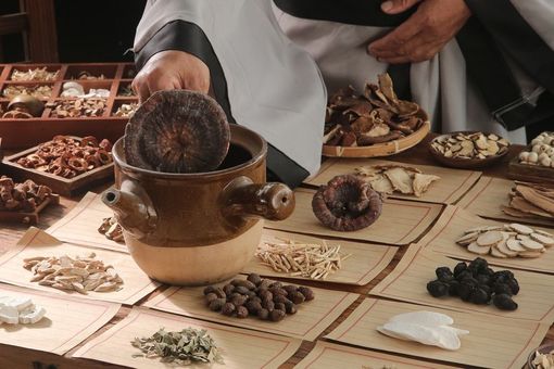 Hands displaying assorted dried herbs and roots on a market table, with a mortar and pestle in the center