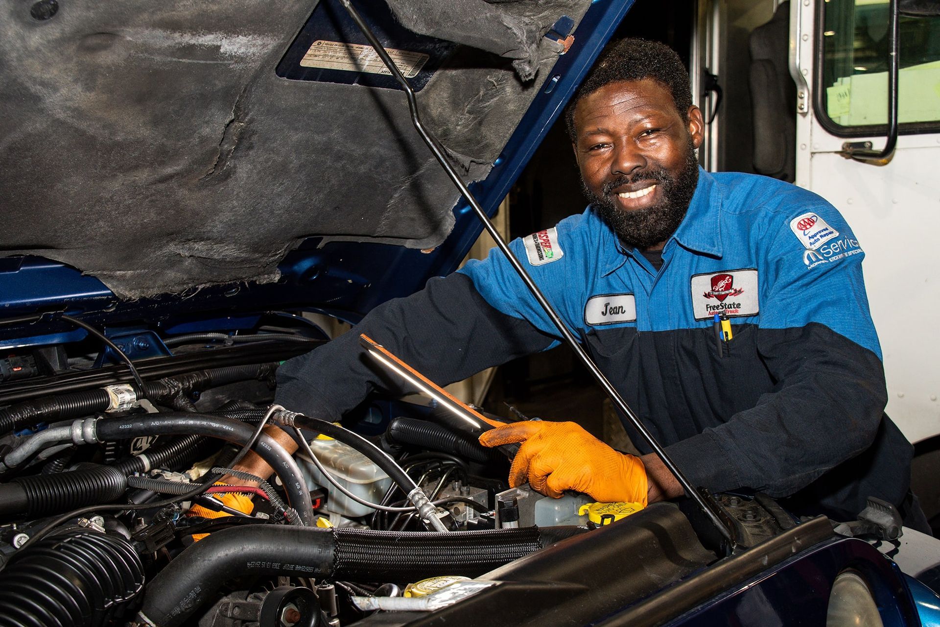 Mechanic working on an engine with a smile. He wears blue work shirt and orange gloves.