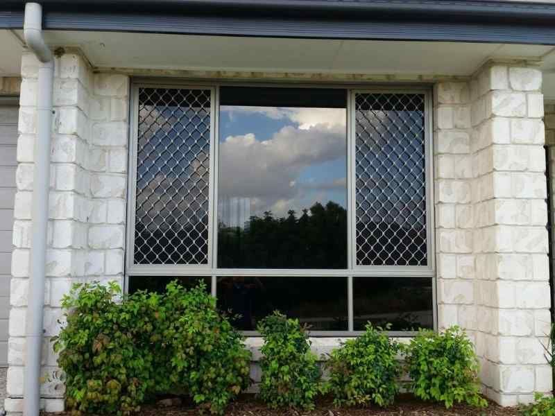 House window with diamond-pattern security screens, stone trim, and shrubs below