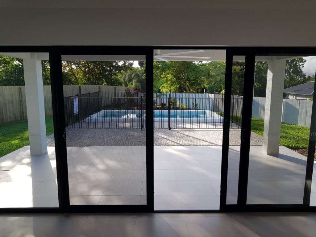 Covered patio with black-framed glass doors opening to a fenced backyard and pool area.