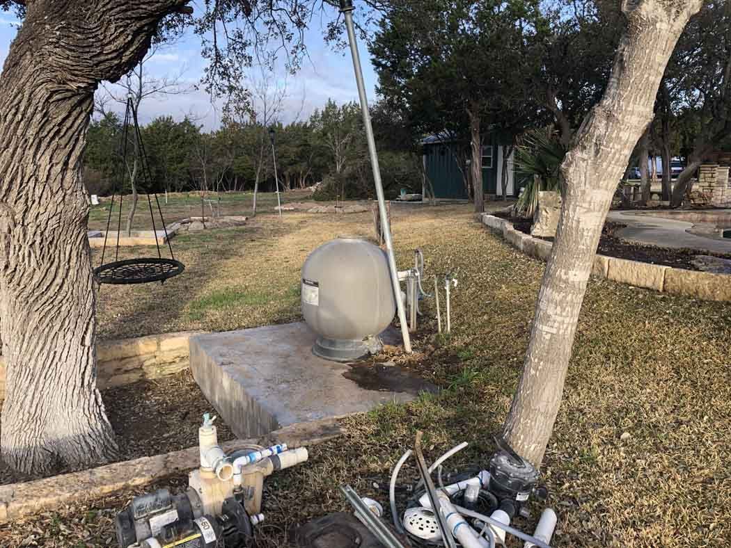 A well pump system on a concrete base, near trees and landscaping in an outdoor setting.