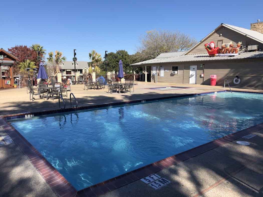 Swimming pool with tables, chairs, and building on a sunny day.