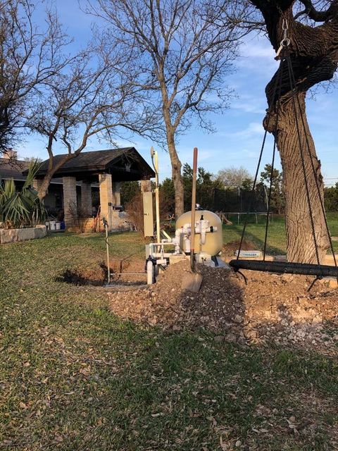 A septic system in a grassy yard, near a house and a large tree.