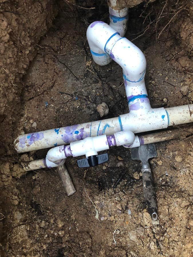 White PVC pipes and fittings buried in dirt, with a black valve.