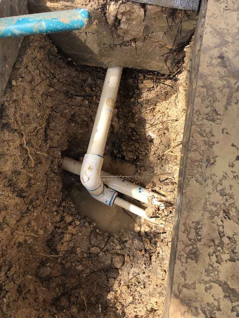 PVC pipes in dirt trench, connected to a concrete structure and blue pipe above.
