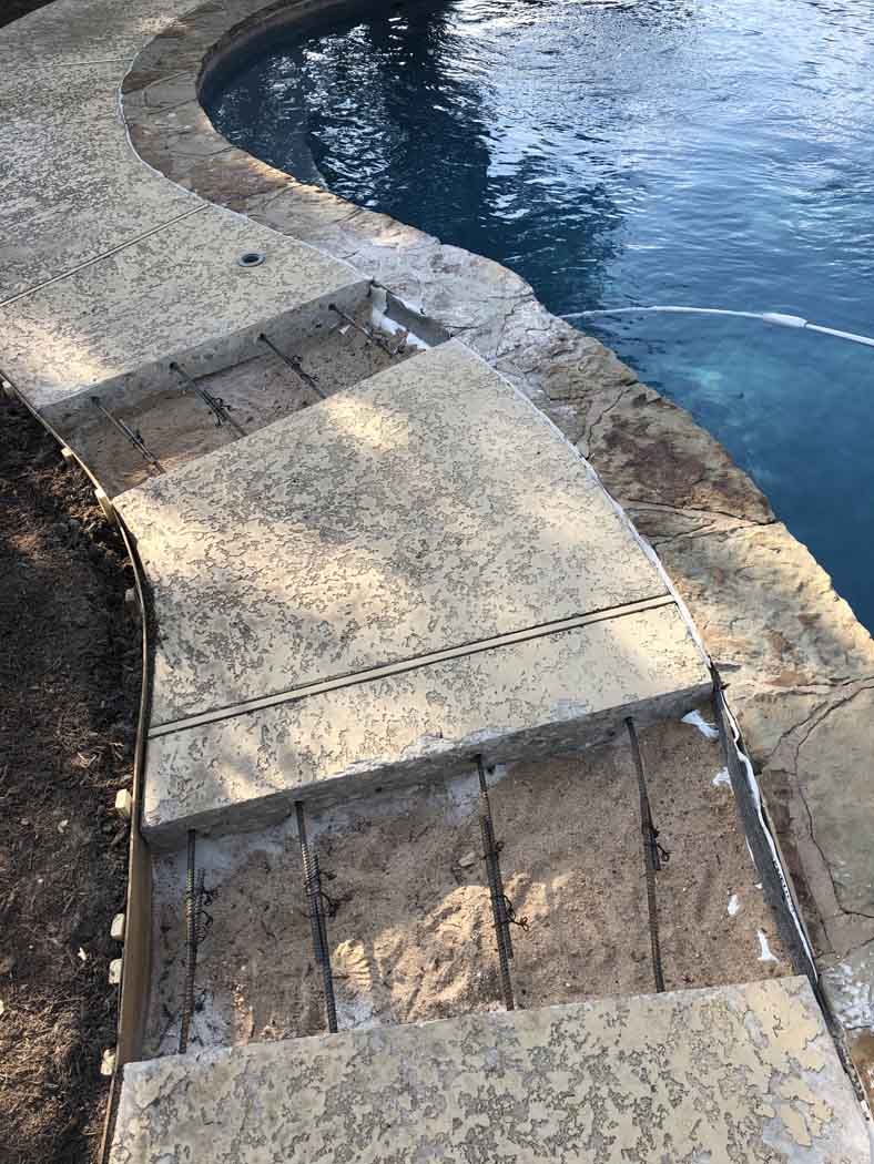 Concrete pool steps leading into a blue pool. Some steps are missing concrete revealing rebar.
