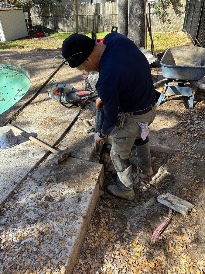 Person using a jackhammer to break concrete in an outdoor setting.
