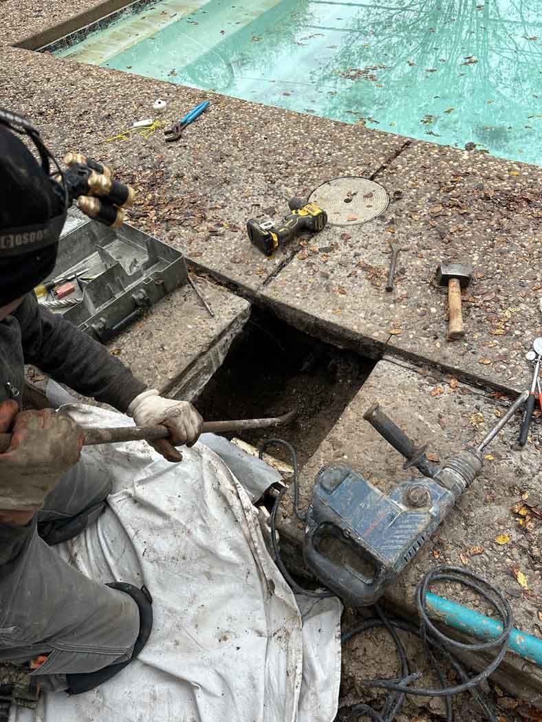 Person using a tool to work on a concrete area near a swimming pool.