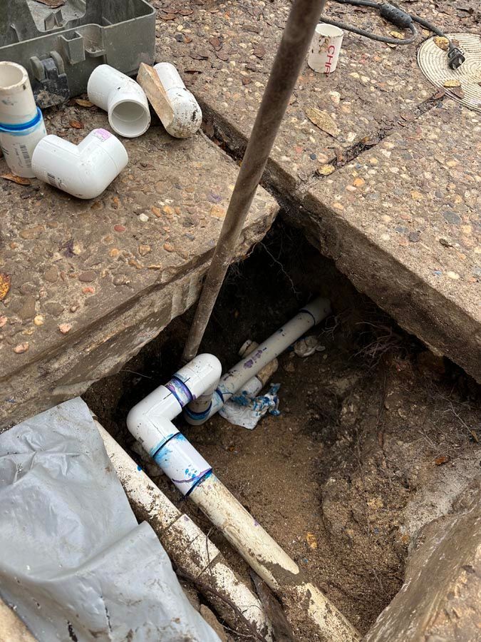 PVC pipes and fittings in a dirt pit, possibly for a plumbing repair.