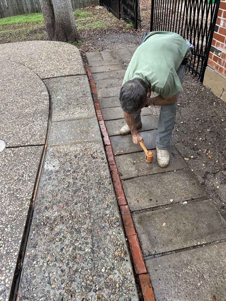 Person using a hammer to work on a brick border of a walkway.