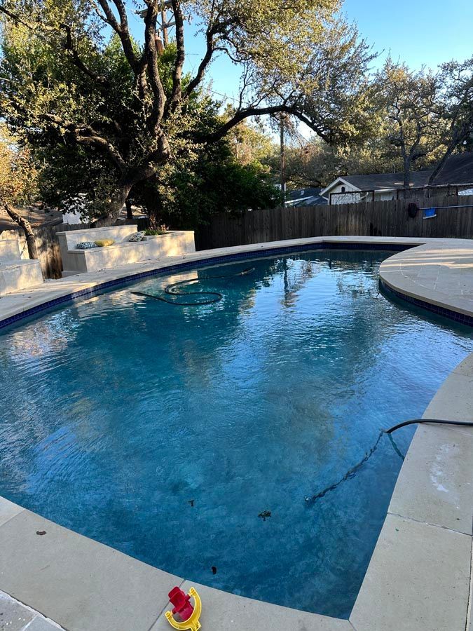 A blue swimming pool surrounded by concrete, in a backyard setting.