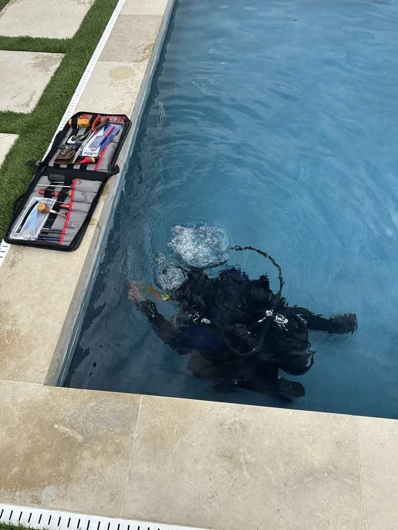 Diver in a pool with scuba gear, bubbles rising. Gear bag on pool edge.