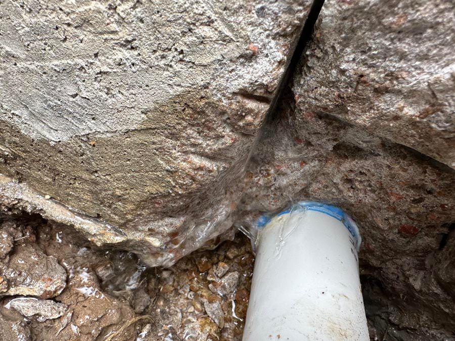 White pipe protruding from a cracked, wet concrete surface. Water drips down.