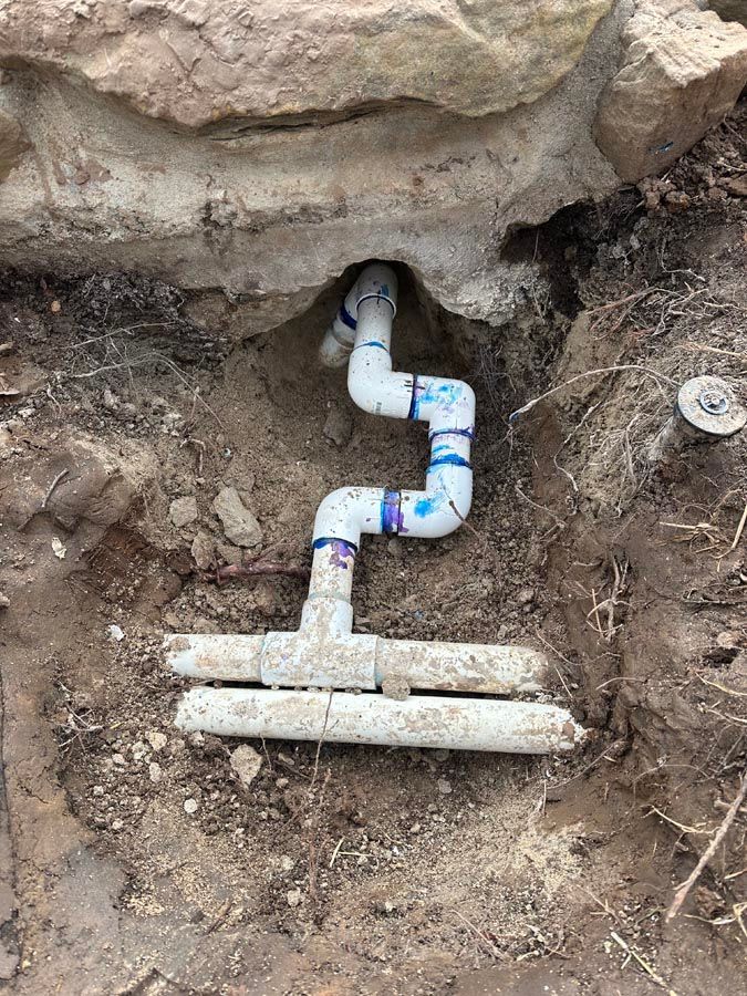 PVC pipes in an excavated area near a stone structure. The pipes form a series of bends.