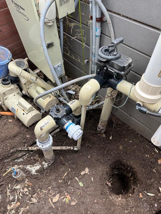 Pool equipment: pump, valves, heater, and plumbing in a dirt setting.