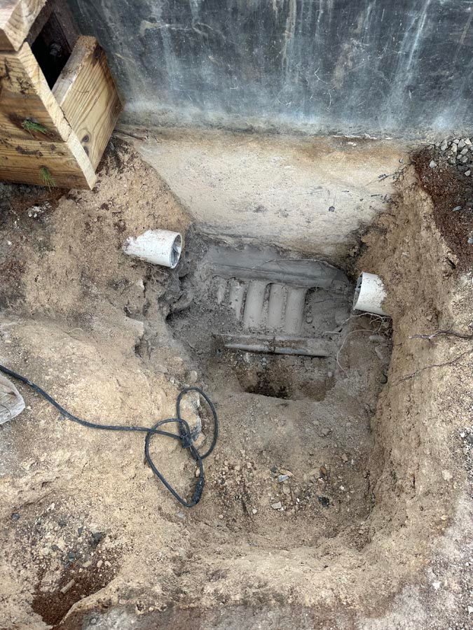 Excavation site with exposed pipes and a drainage system; dirt and sand.