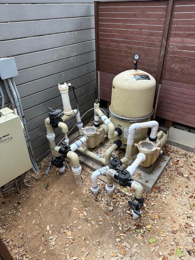 Pool equipment with pipes, valves, and a beige filter tank on a concrete pad.