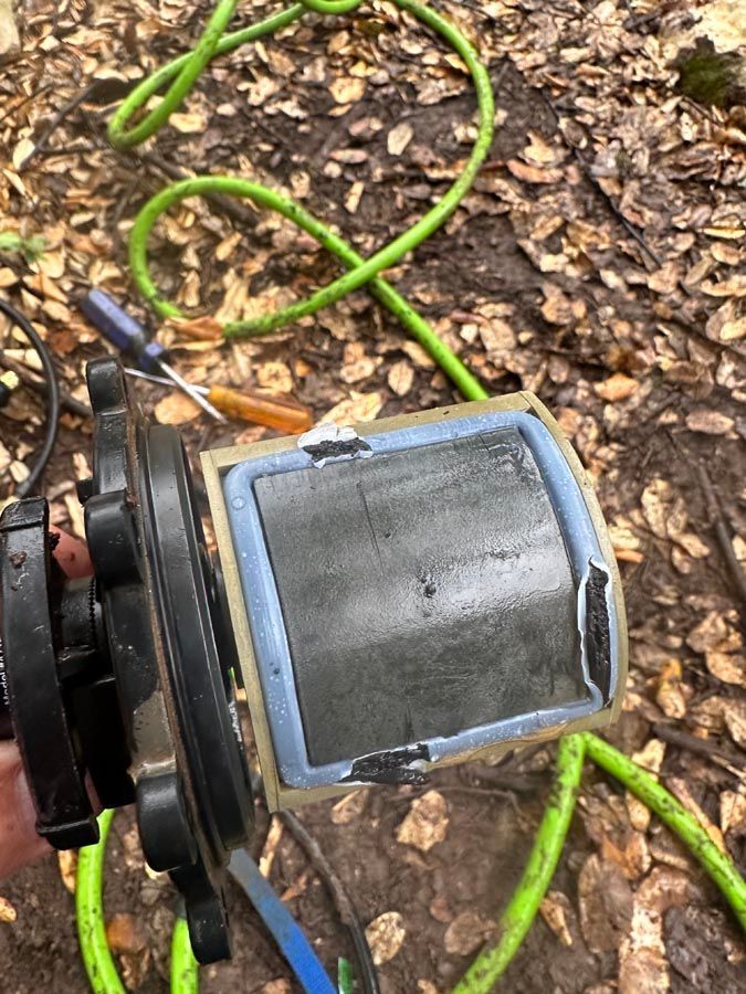 A pump filter with a blue-edged, black filter. Green hose and dead leaves in the background.