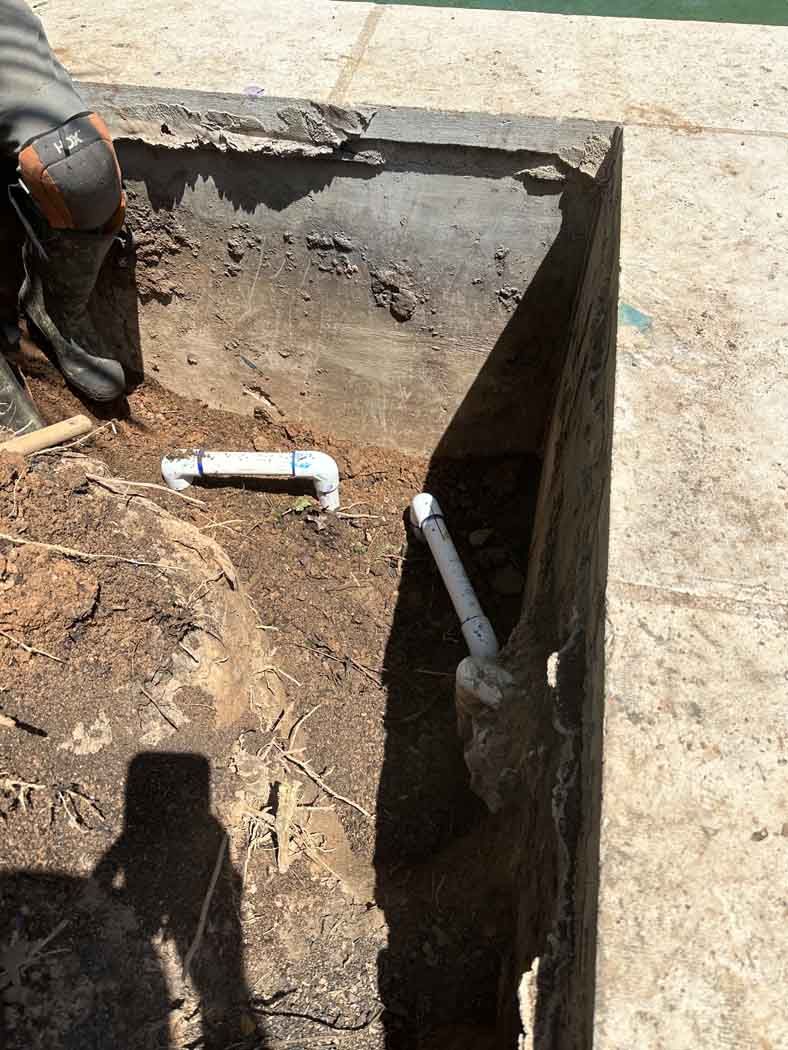 Trench dug near pool edge with PVC pipes and a person kneeling at the side.