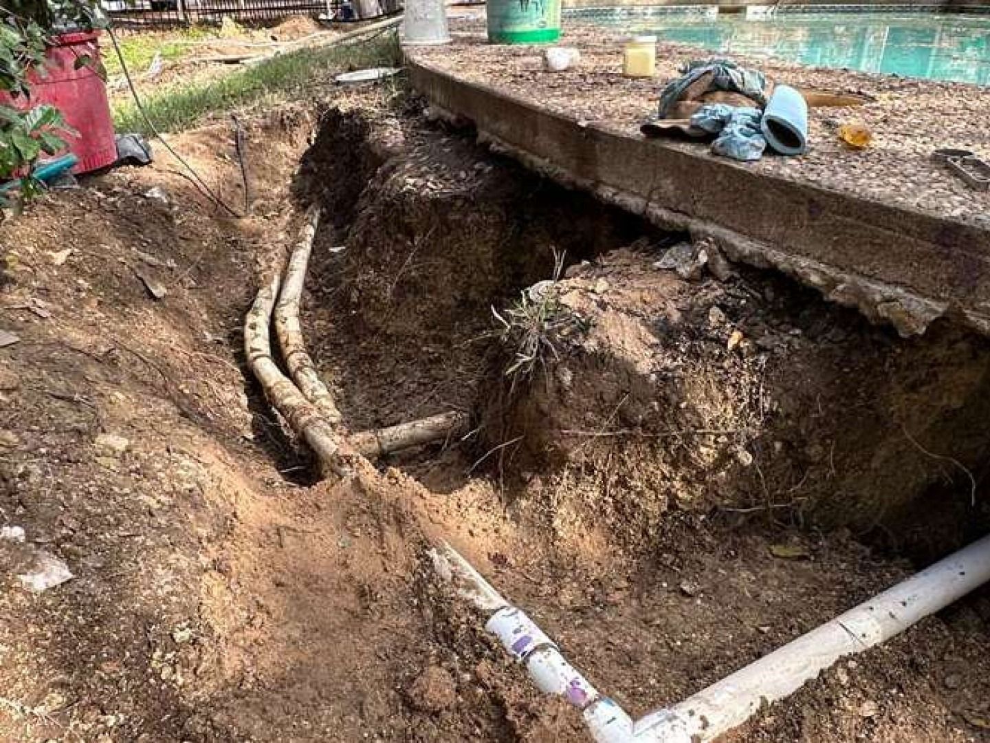 Excavated ground reveals PVC pipes near a pool, with dirt piled around them.