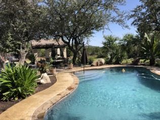 Pool with turquoise water, patio, and landscape under a blue sky.