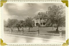 Historic photograph of a large two-story house surrounded by trees and a front lawn.