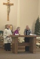 Three people stand at a church altar beneath a crucifix during a service.