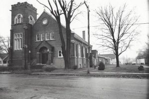 Black-and-white photo of a brick church on a street corner with bare trees nearby